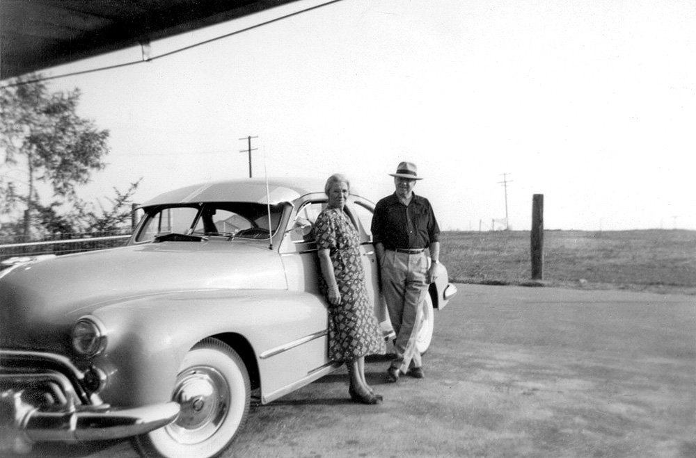 Uncle Alec, Aunt Irene, and their Hog of the Road. "1949" is written on the back of the print.  Uncle Alec was partial to the biggest, most powerful Oldsmobiles money could buy.  He bought a new one every two years.

Although the year is 1949, I am pretty sure the model pictured here is a 1948 Olds 98 Club Coupe.  If it is a 1948 it has the old 115 horsepower 257 cubic inch flathead straight eight, and not the cool new 135 horsepower 303 cubic inch overhead valve V8.  The Olds Rocket, as the new V8 was called didn't come out until 1949.  Don't fret, Unca Alec, as I always called him, would have a new Rocket V8 within a year.

As I mentioned, Alec liked the big Oldsmobiles.  My favorite was his '63 Olds Starfire two door hardtop.  It was electric blue with four bucket seats, a brushed chrome center console that ran down between the two rear buckets and on to the front and up into the dash.  It had a 330 horsepower 394 cubic inch V8. I think it was the one that had a speedometer with a thermometer-style bar that would change from green to yellow to red as it traversed from left to right across the miles per hour numbers.  It might have been his '57 that had that trick speedometer, but I remember he used to joke that after it turned red and passed the 125 miles per hour mark, the radio would come on and play "Nearer My God to Thee."

He finally gave up on Oldsmobiles and went to Chryslers in 1972.   Kelly Motors, the local Sonora Olds dealer used to insist on placing big bumper stickers that had two green shamrocks and said "Buy Kelly Cars." on each car they serviced. As clever as that motto is, my uncle insisted on the service shop leaving his bumper unsullied by any such frivolous B.S.

Well, the fools at Kelly Motors either insisted on, or inadvertently put a set of matching "Buy Kelly Cars" stickers on the back bumper of his car.  Not only that, John Kelly refused to have his slaveys remove them when Uncle Alec told him to.

So, Alec told John Kelly to go to hell and assured him that he'd seen the last of Alec Brady at his dealership.  He peeled out of the driveway, now remember, Alec is 83 at this point, blasts up to the Opera Hall Garage and trades his year-old Olds in on a brand new Chrysler Newport two door hardtop.  Later after the next meeting of the Lions Club, where Alec was known as "King Brady," he invited John Kelly out to the parking lot.  No, not to fight, but to admire what Alec assured John was the first of what would be a whole line of Chryslers, purchased each and every even numbered year, instead of every odd year, as he had when he was an Oldsmobile man. View full size.