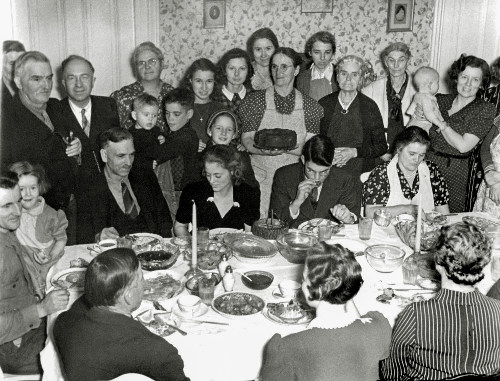 Baugher family, Elkton, Virginia. Christmas Eve, 1939. Seated facing the photographer: my grandfather, my dad's sister, my dad and my grandmother (seated, wearing the apron). I understand that she was a very skilled cook. The cake must have been a good one - it takes center stage. View full size.