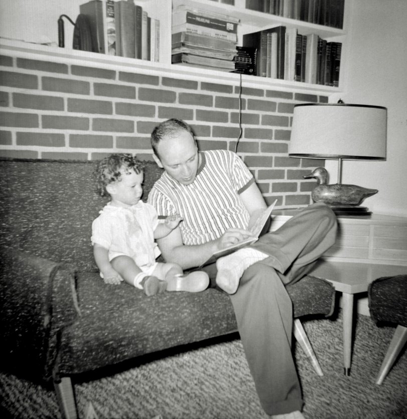 Another look at the original mid-century modern furniture and giant fireplace wall that was in the Levittowner model of the Levittown, Pennsylvania homes as my father reads a book to me. The last time we saw this book shelf it had my parents' original AM-only radio on it. By the time this picture was taken that radio had been moved to the kitchen and a second radio, which received only the new FM high band, was purchased and placed in this living room. I have no memory of them ever listening to that radio. In this era there were very few stations on it and they tended to be stuffy educational affairs, playing classical or jazz music and dry talk shows.
My parents cared so little for this radio that when we moved to our next house in 1962 they gave it to me for my bedroom. The FM programs it received were as uninteresting to me as they were to my parents. But the FM high band was between channels 6 and 7 on the television frequency, and this radio got both channels 6 and 7 on its ends. So when I was told I could no longer watch TV because it was bedtime, I turned on my FM radio, from in my bed and listened to TV.  Specifically I remember I liked to listen to Bewitched. My parents never figured that one out, though I don’t think they would have cared if they had known. View full size.
