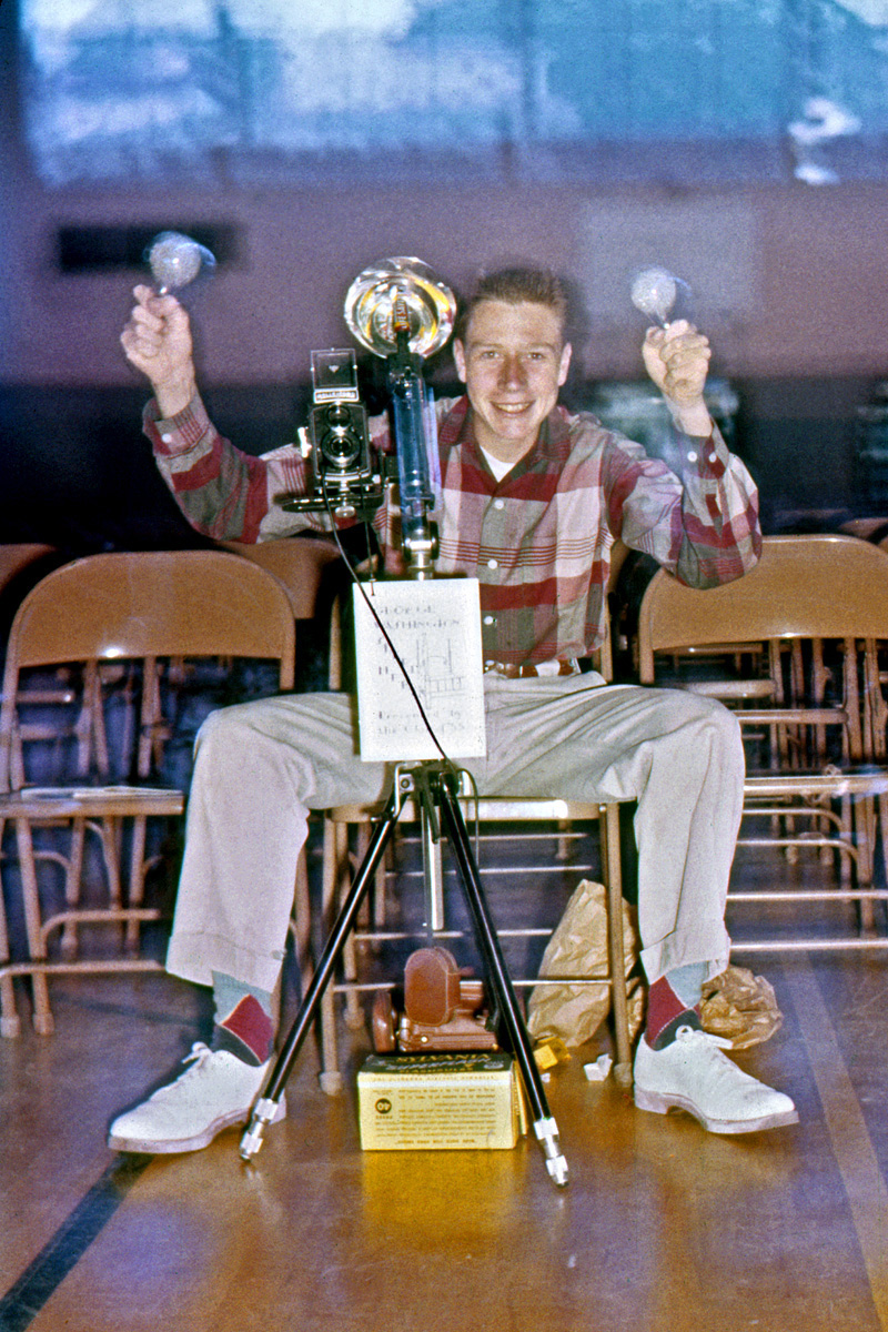 One of my brother's high school classmates. With his Rolleicord, cable release, tripod, light meter and box of Sylvania Superflash flashbulbs, he's obvioulsly the school's go-to guy for photography. The white thing hanging on the tripod is a program for the senior play, "George Washington Slept Here," and he's here in the gym/auditorium to shoot a dress rehearsal. So's my brother, unofficially, with a roll of Ektachrome in his camera. This is a double-exposure, first shot without flash, explaining the phantom images around the bulbs and on the flash unit mount. Doesn't explain why there's a roll of Life Savers in the flash unit, though. Does add a little color interest to it, however. Oh, and I love his clothes, seriously. View full size.