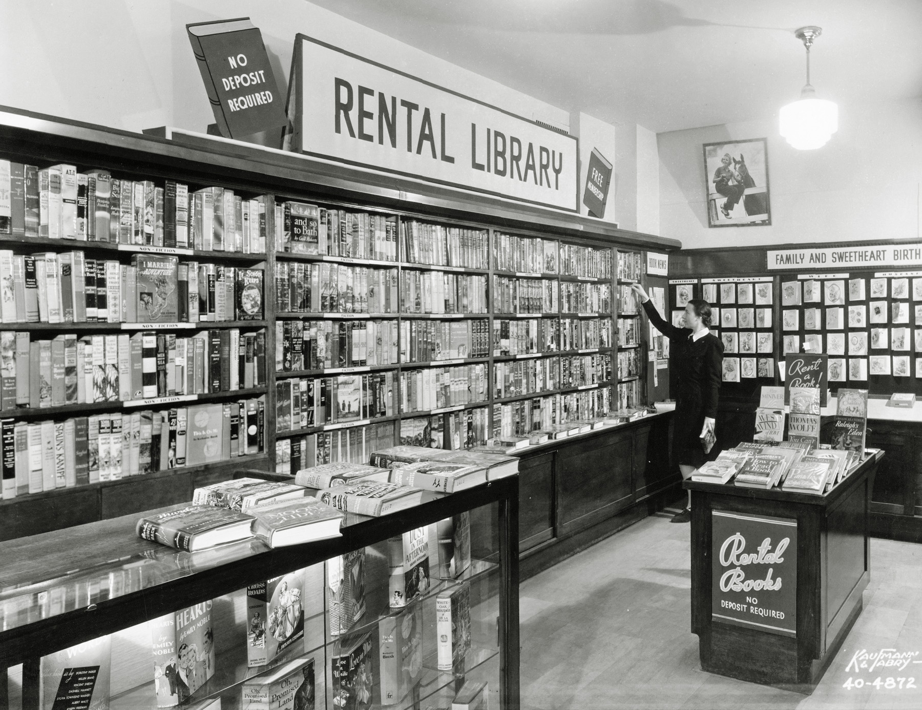 Circa 1940: In an effort to generate more foot traffic in his Chicago camera store, my grandfather Edwin Shutan dedicated a section to a book rental library and hired a staff librarian, Miss Michaels (shown). Edwin charged just 10 cents for three days with no deposit or membership required.  His library was immaculate and well-stocked with all the latest titles from authors such as Thornton Wilder, Alexander Woollcott and Lloyd C. Douglas, to name a few. View full size.