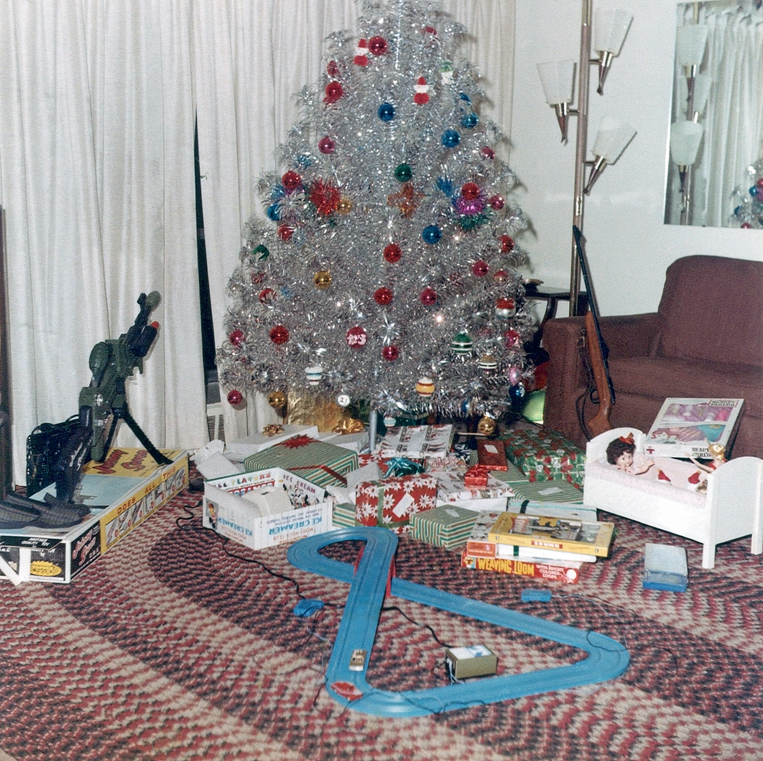 It’s Christmas 1964: snow lying heavily on the ground, gifts under the tree and the house redolent with the evocative aroma of … aluminum. I believe my parents agreed to buy this tree so that Mother wouldn’t be vacuuming up pine needles until Easter.  I still have this tree, (and the color wheel) although it’s not quite as fluffy as shown here.  My parents had a policy that the un-wrapped gifts came from Santa, so this photo must have been taken on Christmas Eve.  Left to right, slippers for Father, a Johnny Seven for one of my brothers and a rudimentary ice-cream maker that came in handy during the Summer months.  On the right is a BB gun that was confiscated by Father later, but my older brother probably consoled himself playing with the slot-car track. Yes, it was a pretty good life in my town of Undisclosed Location.  Oh, me? I got the dolls and cradle shown on the right.

Merry Christmas to my fellow Shorpy-ites. View full size.