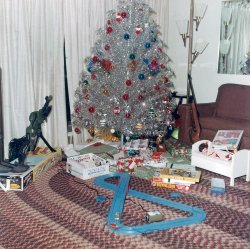 It’s Christmas 1964: snow lying heavily on the ground, gifts under the tree and the house redolent with the evocative aroma of … aluminum. I believe my parents agreed to buy this tree so that Mother wouldn’t be vacuuming up pine needles until Easter.  I still have this tree, (and the color wheel) although it’s not quite as fluffy as shown here.  My parents had a policy that the un-wrapped gifts came from Santa, so this photo must have been taken on Christmas Eve.  Left to right, slippers for Father, a Johnny Seven for one of my brothers and a rudimentary ice-cream maker that came in handy during the Summer months.  On the right is a BB gun that was confiscated by Father later, but my older brother probably consoled himself playing with the slot-car track. Yes, it was a pretty good life in my town of Undisclosed Location.  Oh, me? I got the dolls and cradle shown on the right.
Merry Christmas to my fellow Shorpy-ites. View full size.
Colored poms?Hoople365,
Those colored poms about the middle of the tree.. Are those ornaments or part of the tree?  
Love It!Oh how I wish I had our aluminum tree with the creaky color wheel. I spent countless hours oohing and aahing at the tree changing from red, green, blue (my fav), and yellow. Such a typical Christmas, always a gun, slot cars, or hot wheels,and dolls. I asked my parents about the tree a few years ago, thought it would be retro cool but sadly they threw it away.  Enjoy it while you can!
Classic 1964 Christmas morning Every little boy on our street wanted a Johnny Seven. How could you resist seven guns in one. The tree is a classic. We actually had the same tree, until our dog destroyed it one Christmas day while we were out.
(ShorpyBlog, Member Gallery)