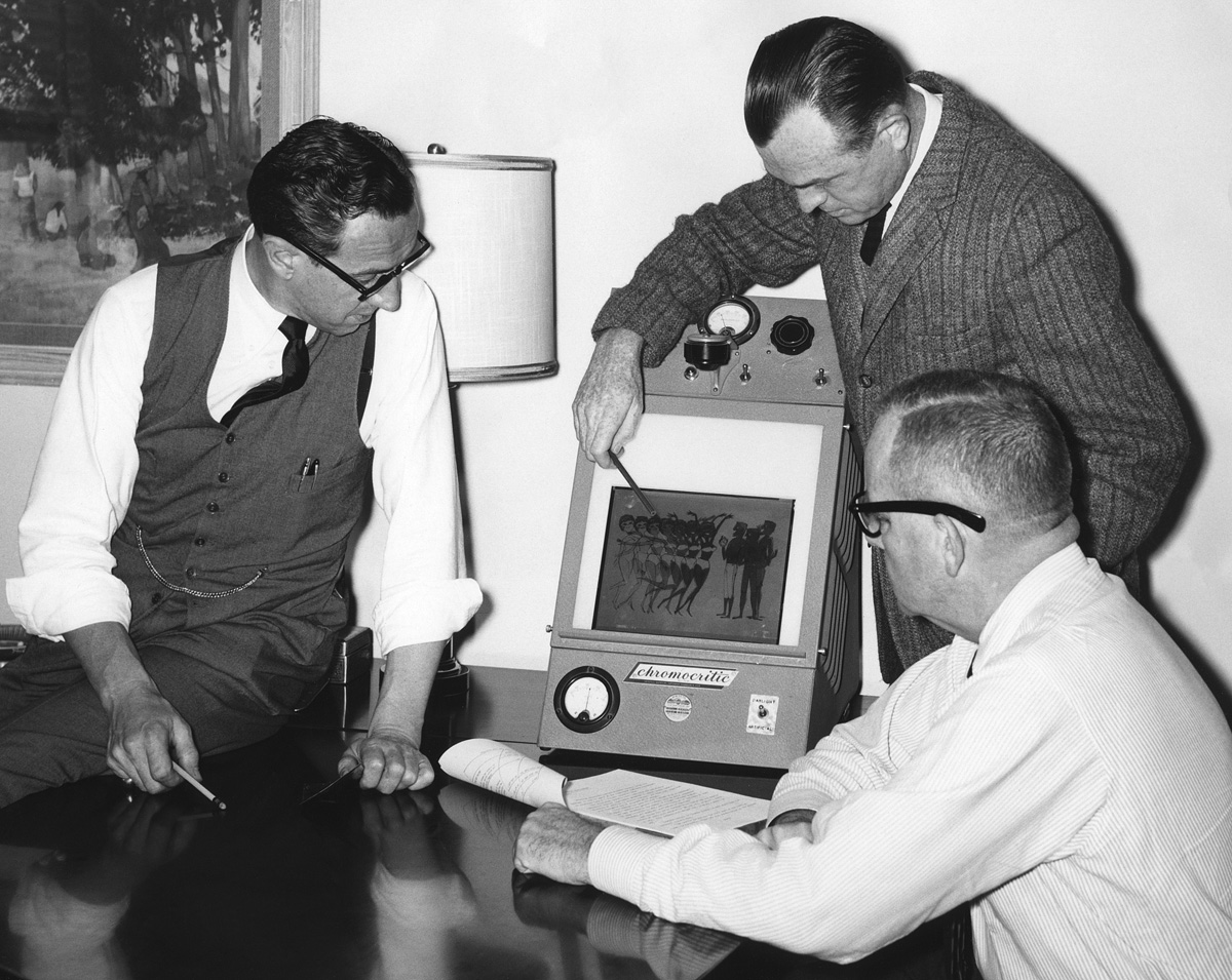 c.1955 c.1959*. Ad men at work with a gizmo. My uncle, at the time vice president and production manager at the Foote, Cone & Belding advertising agency's San Francisco office, is at left. The gizmo is a "Chromocritic," a term which up to now returns zero hits on Google, so here's another first for Shorpy. It's obviously something used for viewing color transparencies under differing lighting conditions; the switch at the lower right toggles between "Daylight" and "Artificial." Extreme magnification reveals that its sole distributor was the Macbeth Arc Lamp Company of Philadelphia, PA. There Google helped me, and they were indeed suppliers of precision-calibrated lighting devices for the graphic arts industry. The graphic itself is in classic mid-50s illustration style. From an 8x10 print in a stash of my uncle's memorabilia I just acquired. *Thanks to Dave and others for narrowing down the actual dating. View full size.
