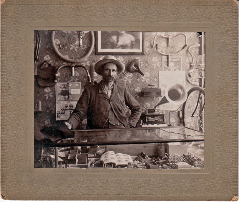 The proprietor of a bicycle shop stands proudly behind the counter in May 1902. Like many bicycle dealers of the day, he carried a sideline of phonographs to generate income in the off-season. A small but handsome Columbia "Type AA" Graphophone with large accessory brass horn is displayed at his side.
