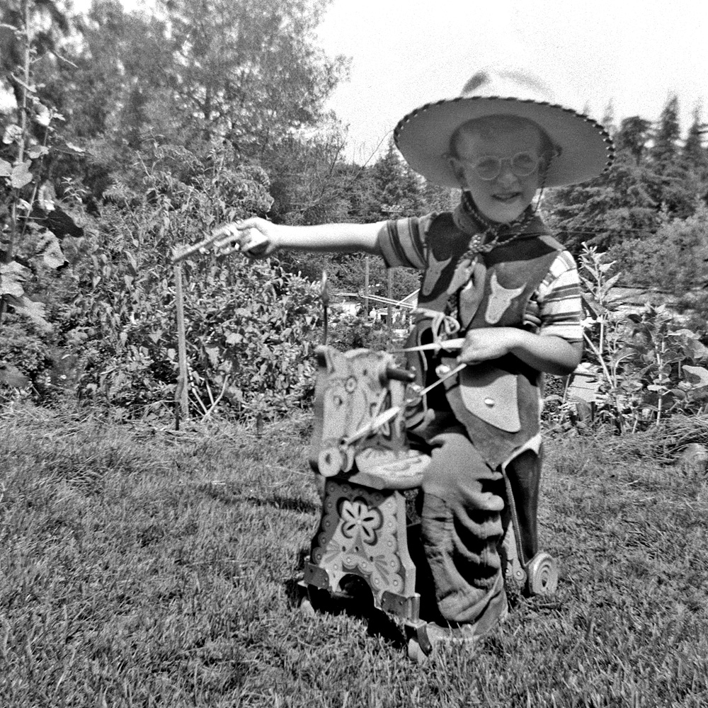 Or, "Smile when you say that, hollyhock!" Me, age 5, in my brother's hand-me-down cowboy hat and vest. I'm pretty sure those are my very own gun and horse, though. And glasses. Taken in what was later our cut flower garden.
