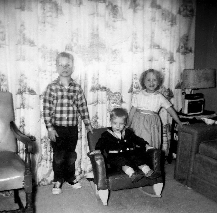 This somewhat faded photo of my siblings and myself was taken, I believe, around Easter 1962 or 1963 at our home on Parkdale Drive in Caseyville, Ill. My younger brother Scott is in his little sailor suit and my sister Cindy is decked out in an appropriate springtime frock. Yours truly, however, is in a flannel shirt and jeans. What I think happened is we were coming home from church and I saw some of the guys playing baseball. I ran ahead and changed quickly so I could join them. Meanwhile, my mom is digging out the camera for the obligatory Easter photo and was quite dismayed that I'd already changed. I heard about it; hence, the glum look on my face while my brother and sister are quite pleased at my discomfort.

The small radio in the right of the photo looks rather insignificant but it provided the soundtrack to our early childhood years. While getting ready for school in the morning, my big brother had it tuned to St. Louis' KXOK so we could listen to the latest rock and roll songs. In the evenings during the summer, my dad had it set to KMOX so we could listen to Jack Buck and Harry Caray announce St. Louis Cardinals' baseball. To this day, I still love the songs we listened to then and Cardinals baseball. View full size.