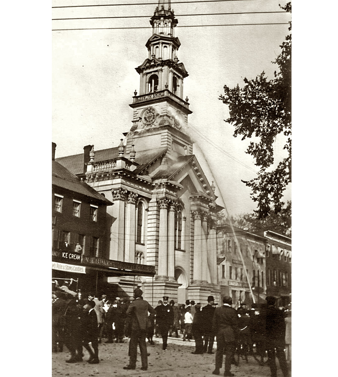 Firemen's practice was apparently an annual event in Keene, NH, c. 1910. This shot was taken by Fred Carpenter at the head of the Square in front of the Congregational Church and Ball's Block. Ball's Block is seen here as a three-story building -- in later days, the top floor would be removed. 