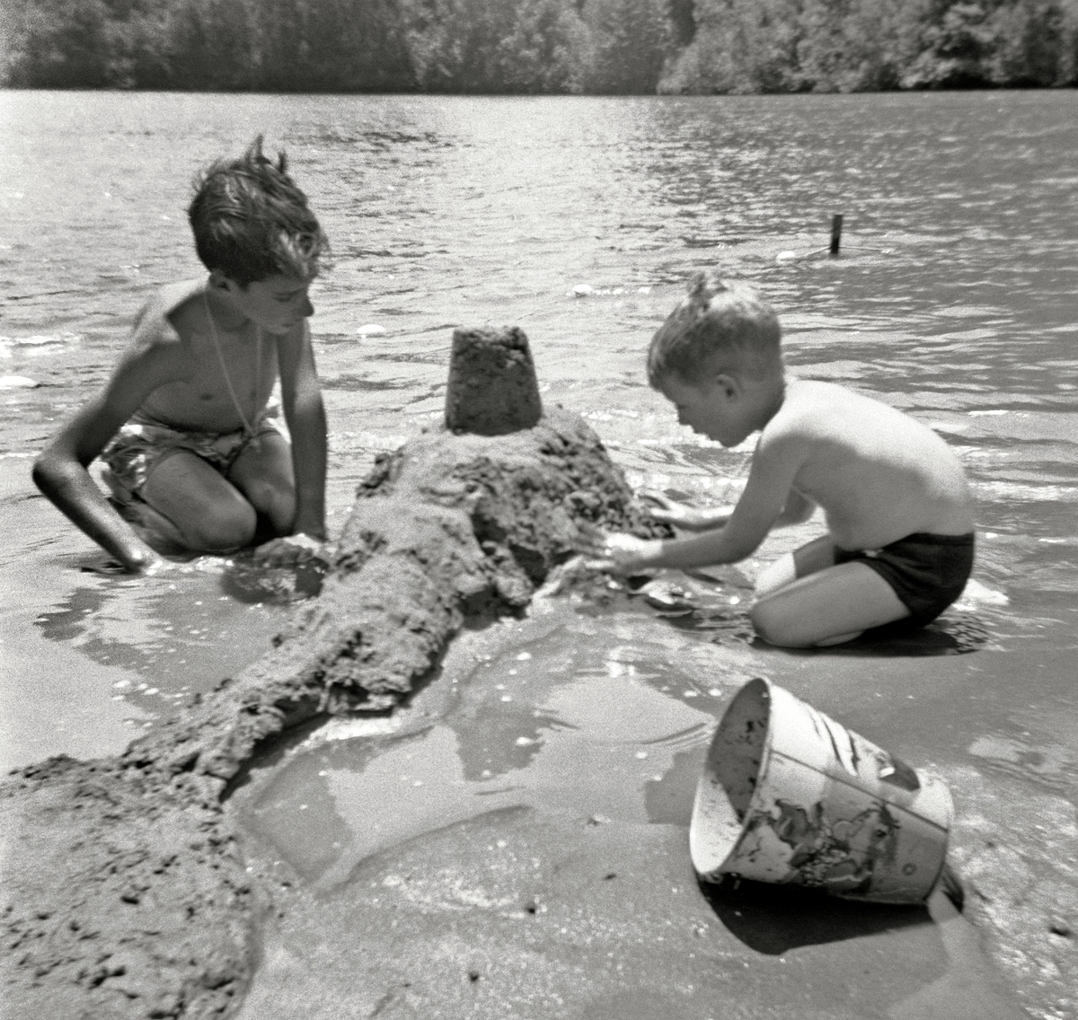 Once again it's time to head up to the Russian River and some vacation fun with the most awesome toy ever to be placed in the hands of a young boy: mud. This is probably around 1950, so my brother is about 13 and I'm about 4 as we put the finishing touches on our impregnable shoreline fortress. Well actually, even more fun was in store when the River Queen motor launch (think Disneyland Jungle Ride boats) came along and its mini-tsunamis destroyed the ever-loving heck out of it. This shot also reveals the limitations of snapshot cameras everyone had to put up with back then, even a comparatively good one like my sister's Kodak Duaflex: we're not really that close but we're still out of focus, and the slow shutter speed meant additional blurriness from just the jiggle of pressing down the shutter release. But with the standard 3x3 print you got back from the drug store, you probably wouldn't notice. Interesting that, proportionally speaking, my gut is roughly in the same state today. View full size.