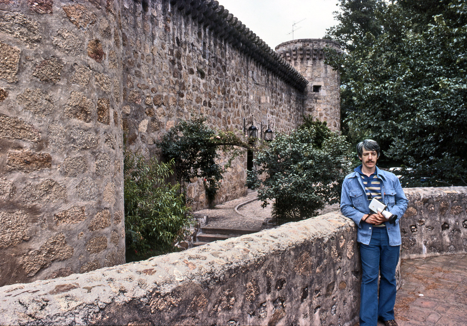 June 19, 1978. Apparently I hit the J.C. Penney men's department immediately before my trip to Spain. At any rate, here I am color-coordinated and looking inexplicably serious with my Nizo Super-8 movie camera at the parador Jarandilla de la Vera, Spain. My friend, who took this Koadachrome slide, and I paid ₧3676 for our one-night double, or about $48 then. Today, the same accommodations seem to be €166, or about $239.  History does not record what Emperor Charles V paid when he stayed here in the 16th Century, nor what he watched on TV. No doubt he was better-dressed.

Now that I think about it, my expression may be the result of jet-lag; this was the day after we arrived. My friend and I tried to avoid it by gradually adjusting our sleep schedule to Europe time for a week or so before departure, staying up later and later each night watching old movies on TV and playing card and board games. It didn't really work. We did document it in a series of rather amusing photos, though. View full size.