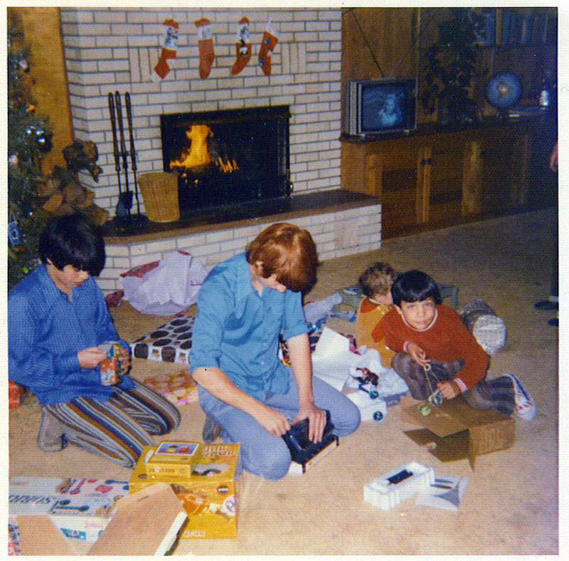My brothers and I opening gifts. I'm the one on the left in the stripped pants. There's a "SORRY" game near me and the yellow box by my knee contains a COX BAJA BUG which was a motorized, gas powered toy that turned out to be a lot of fun. There was no RC for this car, you just chased it down and turned it back the way it came. You could lock the front tires to various degrees of turn to keep it in a smaller area. Don't know what my older brother is checking out but one of my younger brothers has a set of CLICK-CLACKS in hand and at least a couple laying next to him. I remember those things being a rather formidable weapon when swung around and flung by a younger sibling. The youngest brother is sitting by a TOSS ACROSS game which is still available in a reworked version. View full size.

- Gary