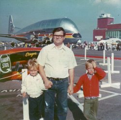 This was back in 1972 or 1973, that's my dad in the middle, I'm on the left suffering from a headache or needing a V8, my brother on his right. I think this air show was at Point Mugu near Camarillo, California. Or at Van Nuys Airport. Despite my unhappy look I loved these shows as a kid. Can anyone help with what kind of cargo plane that is in the background?
NASA Super GuppyNASA "Super Guppy" transport.
NASA Super GuppyThe Super Guppy, the smaller Guppy, the civilian Stratocruiser and its military counterpart the C-97 were all based on the WWII Boeing B-29 Superfortress bomber. The B-29 had four Wright Cyclone R-3350-R23 turbocharged engines. The early Guppy was equiped with four Pratt &amp; Whitney R-4360's, the Super Guppy is Allison 501-D22C turboprop-powered.      
It&#039;s a Supper Guppy.It's a Supper Guppy. - Mike
[As opposed to the earlier, less successful Breakfast Guppy. - Dave]
The earlier GuppyThe previous Guppy was the Pregnant Guppy which I saw at the airport in Long Beach, California, sometime shortly after it made its first flight in 1962. Aero Spacelines used surplus KC-97 Stratotankers for the basic building blocks. The PG was really something to see taking off. The Long Beach airport at that time was still a major aviation center and one of the busiest in the world, but today nobody wants an airport in their backyard (so don't buy a house near the airport!)
S-IVB TransportNASA used this plane to transport the third stage of the Saturn V, called the S-IVB, from the plant to the Cape.  It was the only stage small enough to be flown - the first and second stages were moved by barge.
StingerThe Formula 1 racer in the foreground looks like Art Williams's "Stinger" race plane. It would have been only about a year old at the time the photo was taken. Pretty sure it is in a museum now. I think its last racer-owner was astronaut Deke Slayton.
More InfoMore info on The Stinger (and a strange tale featuring Deke Slayton's ghost) can be found here.
I was there too!Yes, it was either 1972 or 1973.  A bunch of us from Northrop Tech in Inglewood drove out to that show.  I clearly remember the F-14 parked next to the Guppy, it was the first time I had seen both aircraft in person.  There was a live fire display at the show, with missiles being fired from an F-4 in front of the crowd out over the ocean.
Flying GuppyThis Guppy was also flown into Huntsville, Alabama.  It flew the Instrument Unit built by IBM to the Cape.  It was a real sight to see it take off.  You'd think it wasn't going to make it.
(ShorpyBlog, Member Gallery)