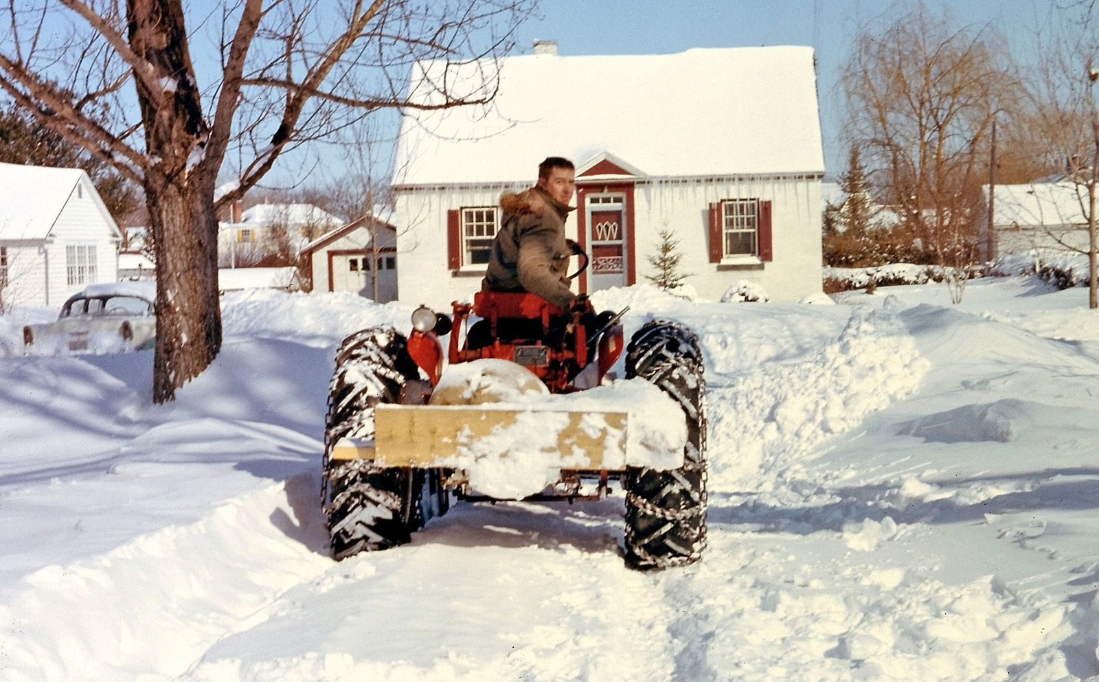 A shot my Dad took in Bedford, Quebec, during a late 1950s winter. Here he's hired a friend with a farm tractor and chains to plow out one of the bigger dumps from our laneway. If I'm not mistaken, the "plow" appears to be a 1 x 12 piece of wood. View full size.