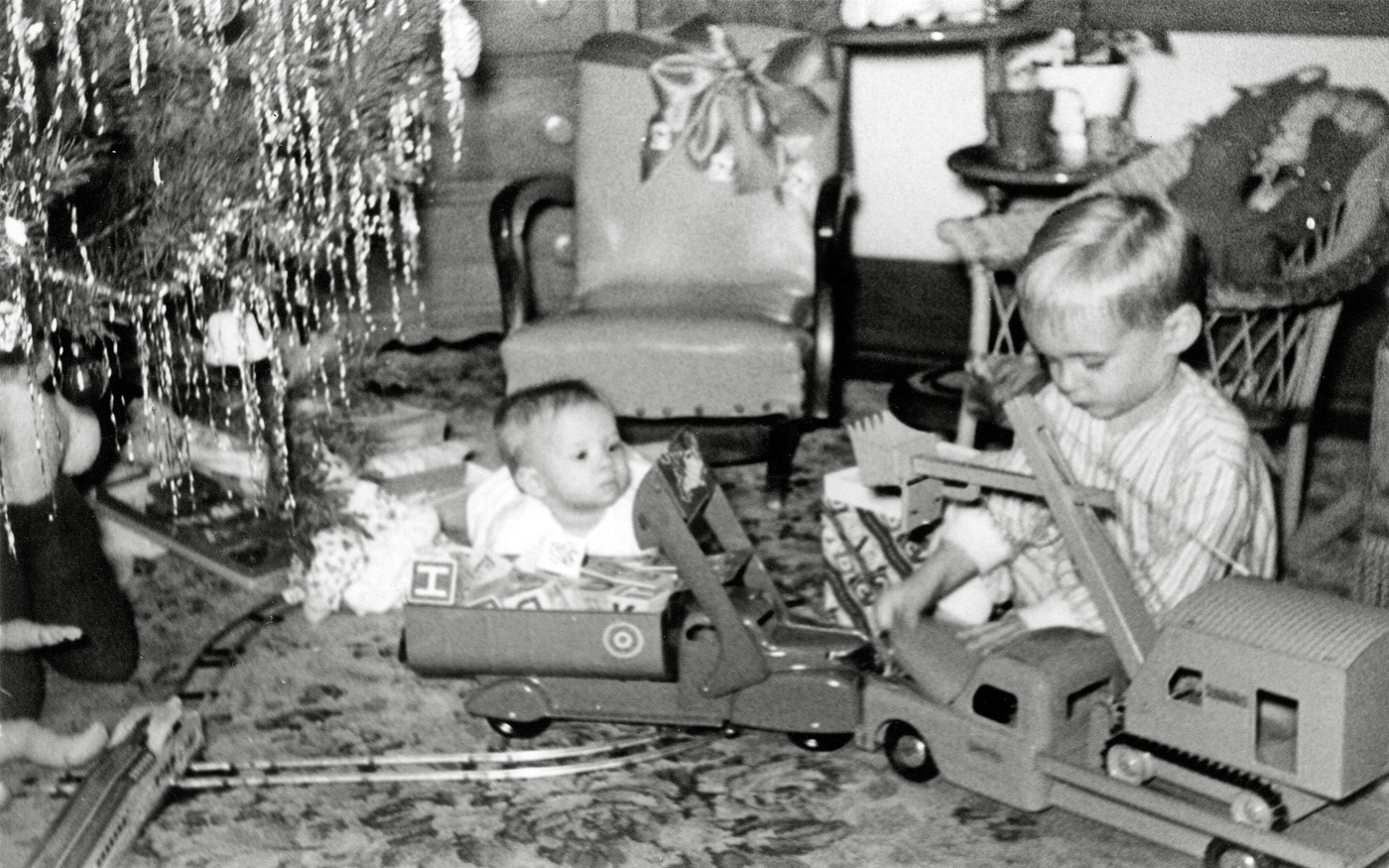 Christmas morn 1949, Hamtramck, Michigan. Amazing what details I remember. My sister is 10 months old. I am checking out the plastic motor under the hood of the truck. When I came into the living room, my parents were already up and had the windup train running around the figure eight track. I stepped on the track and derailed the train. The kid-sized rocking chair in the center was covered in yellow vinyl. It suffered a sudden end a few years later when a table lamp fell on it melting a hole in the plastic. I still remember my Mom's panic and and seeing the excelsior stuffing where the plastic melted away. The picture was taken with my Father's trusty Argus C-3 which used large flash bulbs which had the same screw in base as a standard light bulb. View full size.