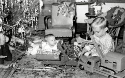 Christmas morn 1949, Hamtramck, Michigan. Amazing what details I remember. My sister is 10 months old. I am checking out the plastic motor under the hood of the truck. When I came into the living room, my parents were already up and had the windup train running around the figure eight track. I stepped on the track and derailed the train. The kid-sized rocking chair in the center was covered in yellow vinyl. It suffered a sudden end a few years later when a table lamp fell on it melting a hole in the plastic. I still remember my Mom's panic and and seeing the excelsior stuffing where the plastic melted away. The picture was taken with my Father's trusty Argus C-3 which used large flash bulbs which had the same screw in base as a standard light bulb. View full size.
(ShorpyBlog, Member Gallery)