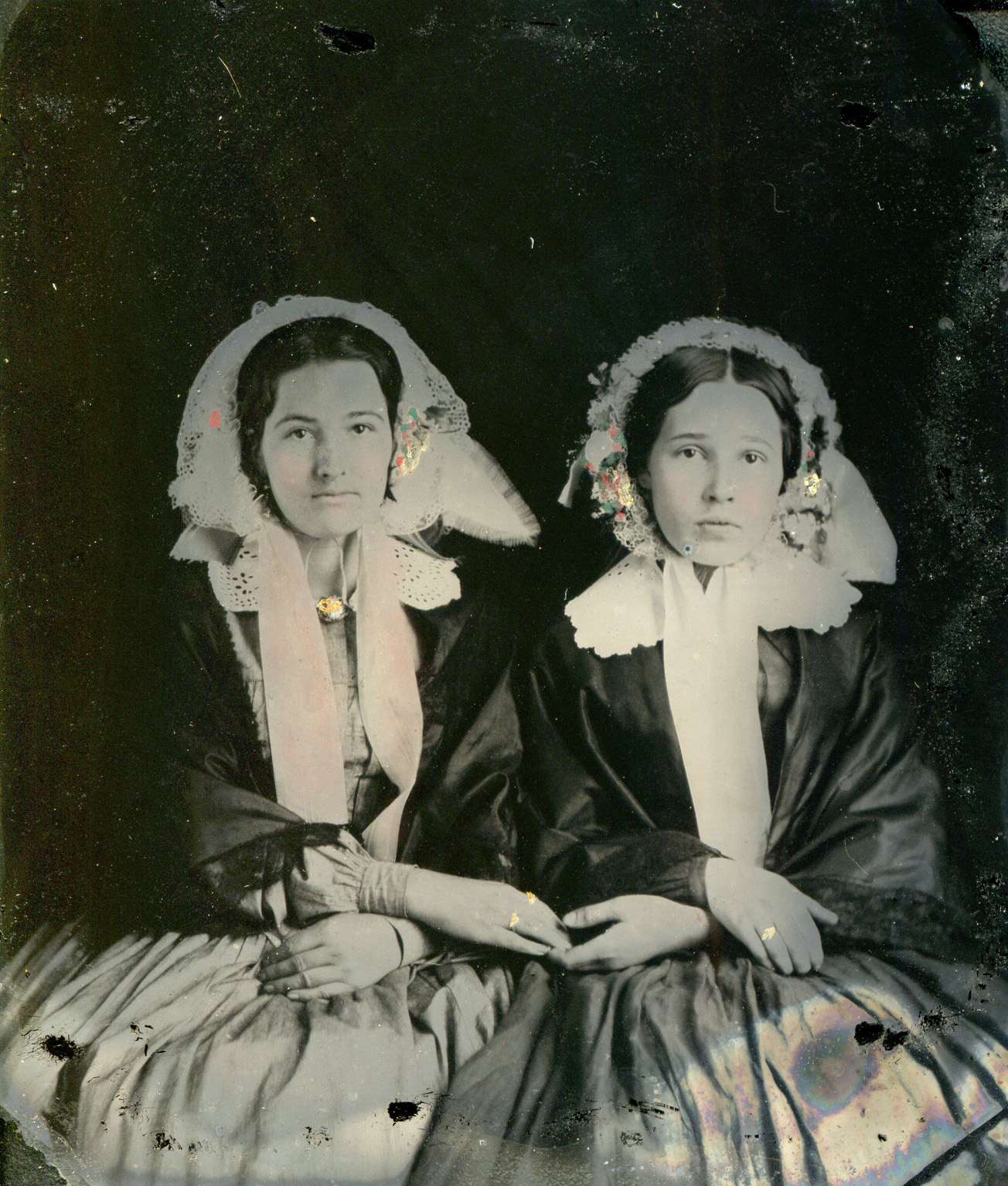 This is a sixth-plate ambrotype (2-3/4" x 3-1/4") on clear glass. Black pigment has been added to non-emulsion side, and color was hand-painted onto emulsion side.  I bought this some years ago an an antique store, and I have no idea who these women are or where this picture was made. View full size.