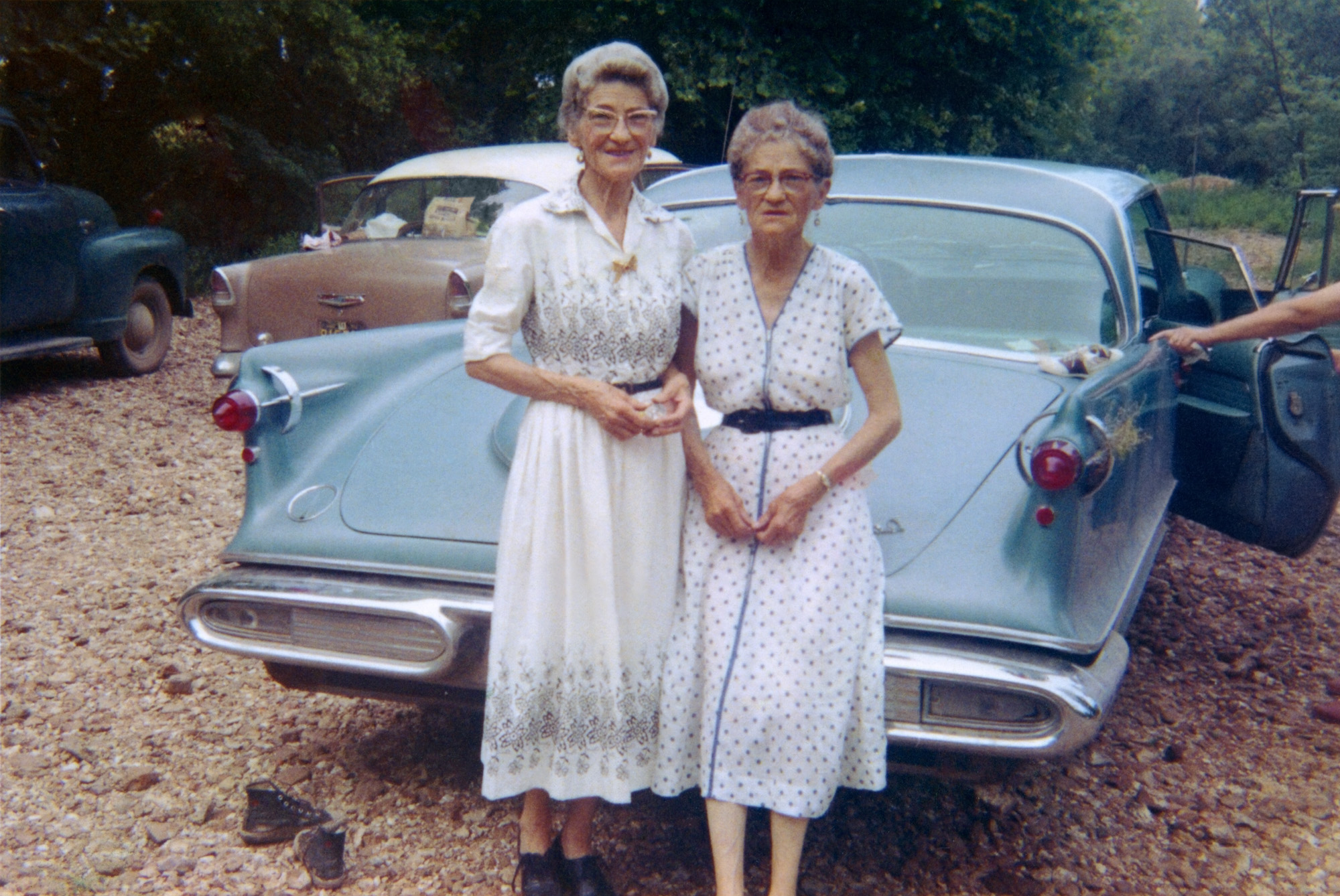 My sister-in-law Gimi's maternal grandmother and her identical twin pose with a 1958 Imperial in this Kodacolor print from July 1959. That's all we know for sure, although Gimi believes this is in the Ozarks of Missouri. Other elements give rise to speculation: the right taillight assembly suggests a close encounter with some native plant life, perhaps on a narrow, winding road that brought us hither. The pointing finger I like to think indicates a voice exclaiming "Get those saddle shoes OFF the Imperial!" As for the other orphan footwear, I just want to say I'd rather not look under the Imperial. On a happier note, a 1955 Chevrolet. View full size.