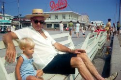 Photo taken at Rehoboth Beach, Delaware, 1970. View full size.
[Uploaded by stonefish. -Ken]
What a nice shotI'll bet he was a great Gramps. I hope your memories of him are fabulous.
I wonder if the salt water taffy place is still around. The East Coast beaches I have visited have a different vibe than those out here on the left coast.
DecadesShows you how much of the 50s look was still around in the 70s - the building, the sign, the strolling family.
Dolle&#039;s TaffyThe sign is still exactly the same. Every time there is a major storm they repair or replace it as quickly as possible. This has been a major trademark and landmark on the Rehoboth Boardwalk since before I was born in '49.
I was born and raised in Delaware and spent much time at both the Delaware beaches and the Jersey shore, and one must make sure to always call them by their proper description.
Having just recently relocated to the west, I cannot yet make any comparisons with beaches on this side of the country.
Good shot and nice hat. 
Family vacationsHey, that's my grandfather and cousin on that bench.  I remember when we went on a family vacation together to Rehoboth.  We stayed in cabins and we had to bring our own sheets.  I remember walking to the beach for pizza.  Family vacations are so important to make happy memories for kids and enjoy family time for the parents.  Look, no iPod or kids texting, just enjoying the wind and sea.  Thanks for sharing the photo. DJ    
I spent summer 2008 inI spent summer 2008 in Rehoboth, was working close to this place in ice-cream store. actually i'm from russia and spent that summer in USA. it was interesting to find out that between 70 and 08 looks the difference is not too big. Lovely photo! 
We couldn&#039;t resist......taking the same shot again in 2016.  The location is staged, wardrobe was coincidental (I apparently dress like a 75 old). 
(ShorpyBlog, Member Gallery, Kids)