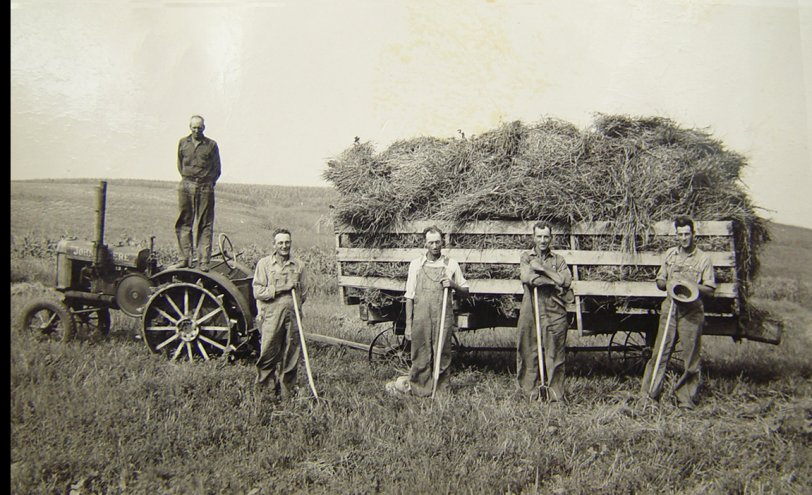 …and Young. My grandfather working (left with rake) at a neighbor's farm – I'm guessing the 1920s. He'd work his farm then also hire himself out to work others in the area as here.
The family homesteaded in Dakota Territory in the 1870s in what is now Union County in SE South Dakota a few miles from Akron Iowa. The homestead was on Bruele Creek, which is mentioned in, and the area is the setting, for the novel "Giants in the Earth" by Rølvaag. Most of the families in the area were Nordic and still reflected that when I'd visit as a child. 
Can anyone ID the year for the John Deere tractor to help place the time frame? View full size.
