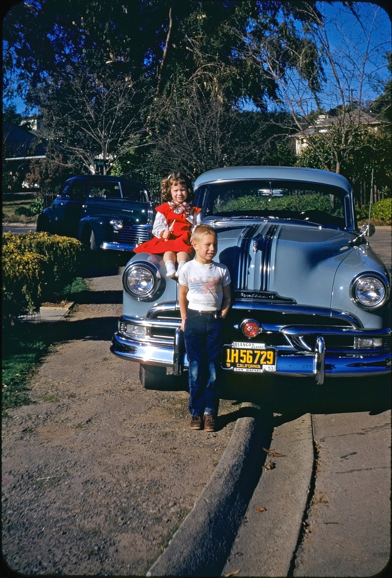 My best friend and his sister with a 1953 Pontiac on a late afternoon in front of their home in Larkspur, California. Since their own family car was the 1941 Pontiac in the background, I'm assuming this shot was taken by the owner of the new one. The dealer, Bianco, was a long-time car dealership in Marin County up through the 2000s. At the time David and I were in the first grade together at Larkspur-Corte Madera School, just three blocks away. Earlier this year you saw us both at his sixth birthday party in this photo. He's no longer with us, but his sister has loaned me her family photos to peruse and has given me permission to post this scan I made of this particularly Kodachromalicious slide. View full size.