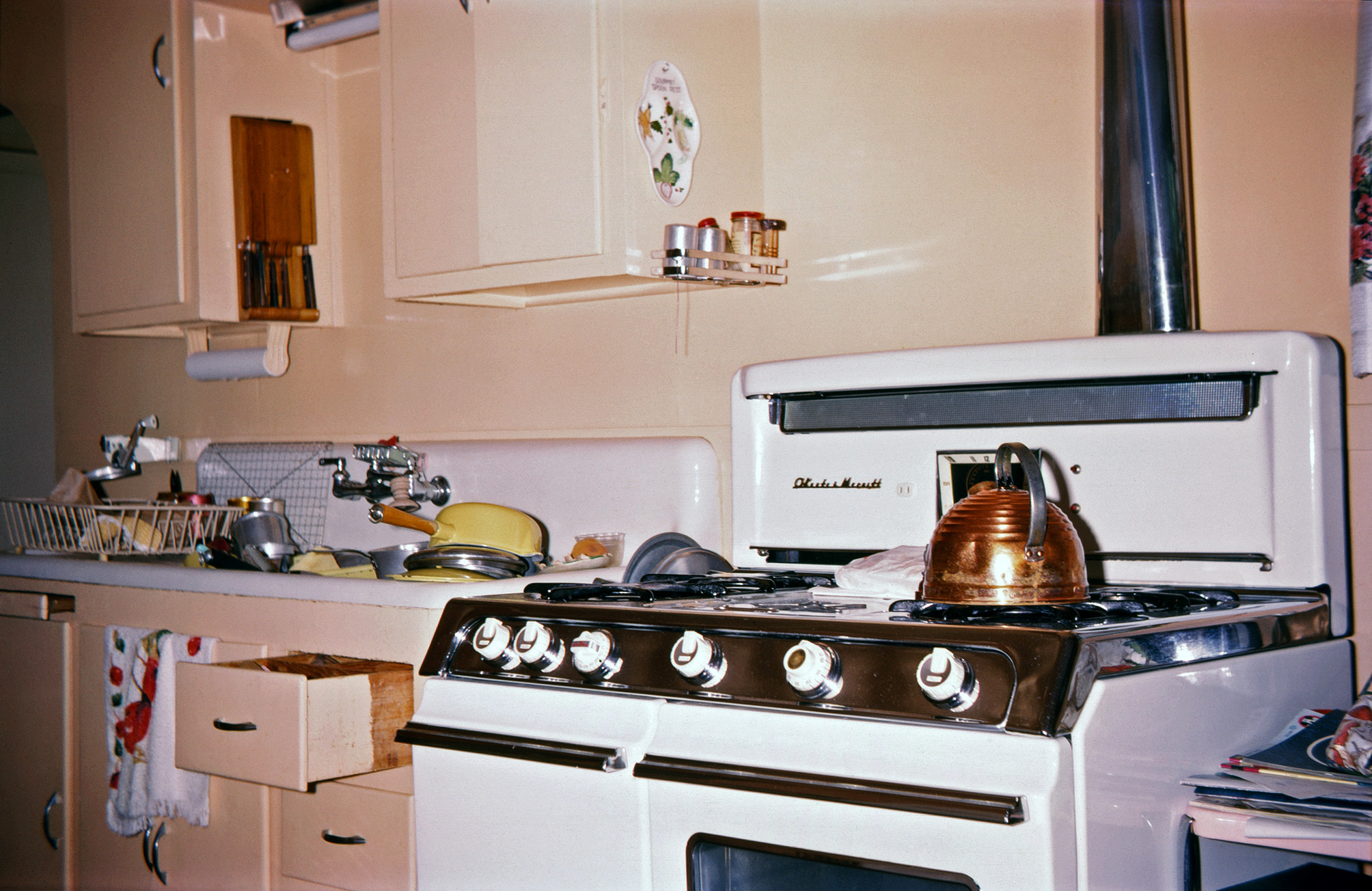 Unless you happened to live in one of those fancy kitchen decor ads like you see over on Plan59.com, your 1964 kitchen might be like ours, a mixture of stuff from the 50s (1955 O'Keefe & Merritt gas range), 40s (sink, cabinets & fixtures from a 1946 remodel) and even the 30s (the copper tea kettle). A package of meat is defrosting on the griddle, which was always a little warm from its pilot light. My Kodachrome slide. View full size.
