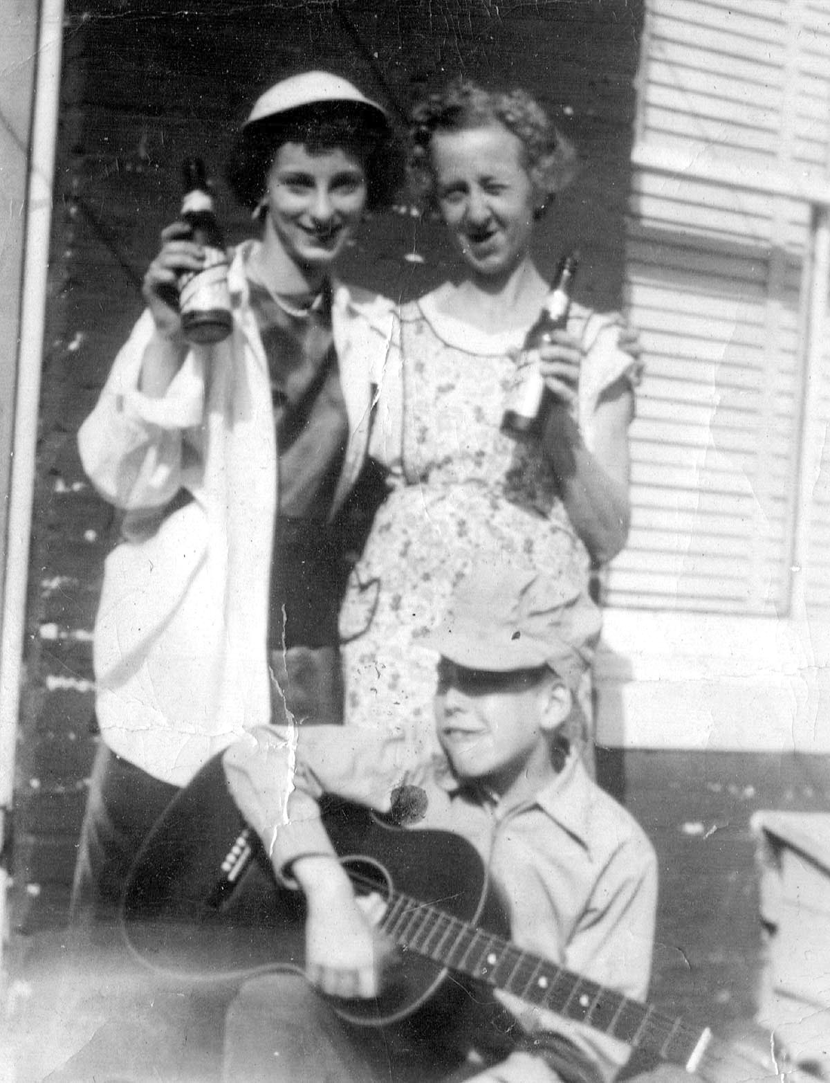 My first crush, Liz, on the left and my mother in her obligatory apron and I strumming the guitar in a poor imitation of the Singing Brakeman, Jimmy Rogers.

The beer is American (a local Baltimore brand) and the RR cap a gift from an uncle who worked as a conductor on the B&O. He had no children and at the end of each run he would check the passenger cars for forgotten comic books for me, which led to the largest collection in my part of the world. And yes in 1959 while I was away in the Navy that sweet lady on the right dumped it.

Picture taken in the rear of the 3300 block of Elmora Ave in Northeast Baltimore, circa 1948. View full size.