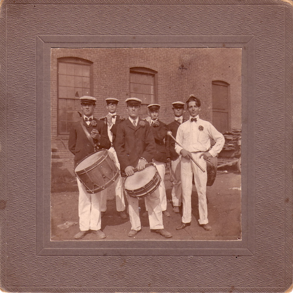 The Keene Matchless Fife & Drum Corps, 1901, posing at the Diamond Match Company factory in Beaver Mills, a complex of mills in Keene, NH. Front: Ed Barrett, Archie Howard, drums; ____ Avery, drum major. Back, F.H. Tyler (my grandfather at age 18), Forest Hall, piccolos; Ben Symonds, bass drum. Beaver Mills was added to the National Register of Historic Places in 1999. It had also housed manufacturing operations including a saw hill, grist mill, furniture mills, and a pail manufacturer.

See an earlier picture of Beaver Mills here: https://www.shorpy.com/node/3235