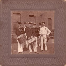 The Keene Matchless Fife & Drum Corps, 1901, posing at the Diamond Match Company factory in Beaver Mills, a complex of mills in Keene, NH. Front: Ed Barrett, Archie Howard, drums; ____ Avery, drum major. Back, F.H. Tyler (my grandfather at age 18), Forest Hall, piccolos; Ben Symonds, bass drum. Beaver Mills was added to the National Register of Historic Places in 1999. It had also housed manufacturing operations including a saw hill, grist mill, furniture mills, and a pail manufacturer.

See an earlier picture of Beaver Mills here: https://www.shorpy.com/node/3235