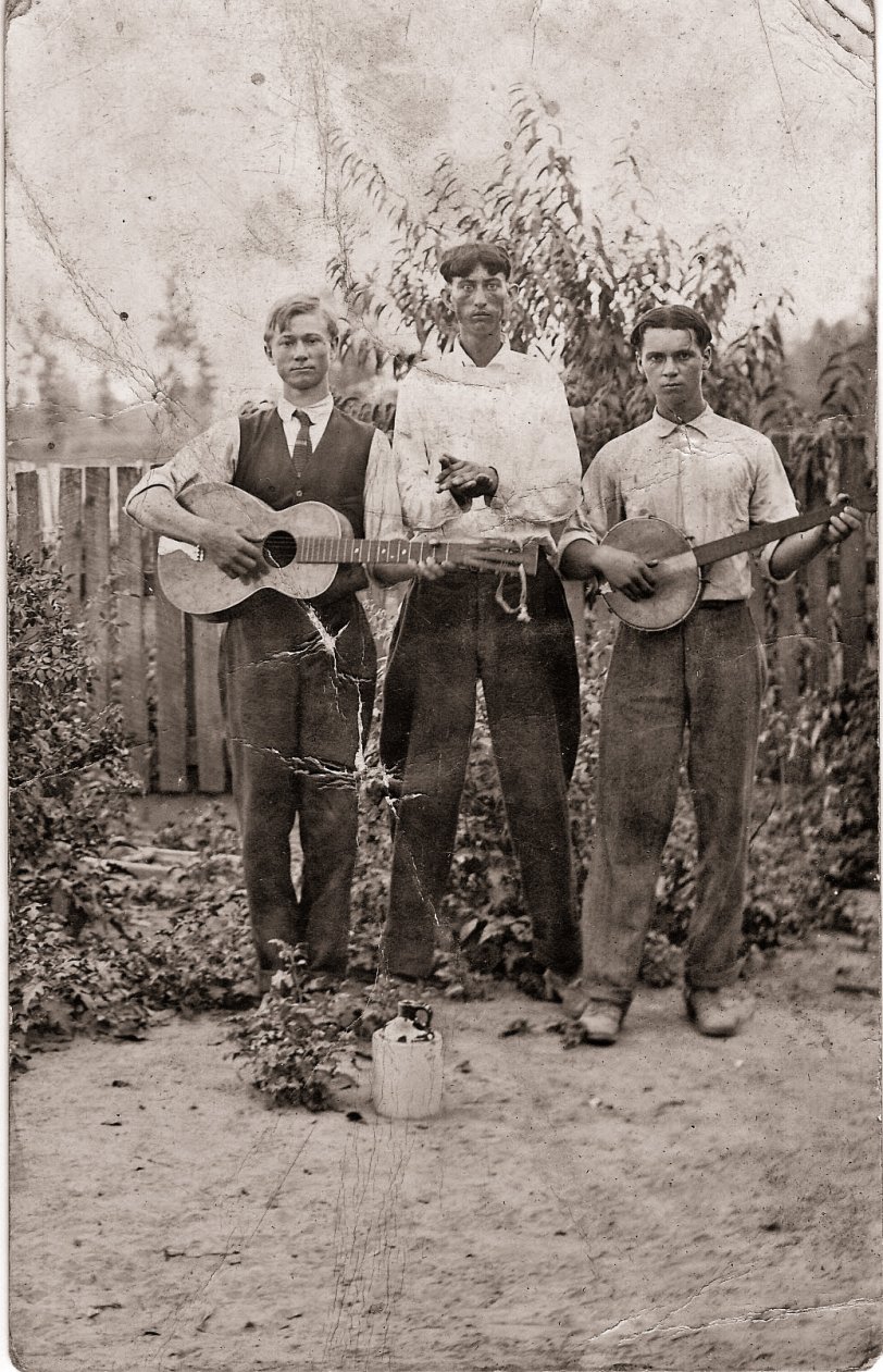 This is a pretty beat-up photo of my grandfather Clyde C. Hooker (1892-1972), center, with those distinctive eyes, and two unidentified gentlemen. I didn't know this picture existed until about four years ago when I received my deceased aunt's and uncle's photo album. Until then I had absolutely no idea Grandpa was musically inclined. I'm assuming he played the harmonica the way his hands are cupped. We think it was taken in the late 1910s or early 1920s around Risco, Missouri. Grandpa was a farmer most of his life and he and my Grandma Maudie raised 12 kids with my dad being the second-youngest. I love the little brown jug in front. Grandpa may have raised a little hell when he was younger but by the time I knew him, he was a strict teetotaler. Of course, it might just have been a prop. View full size.

