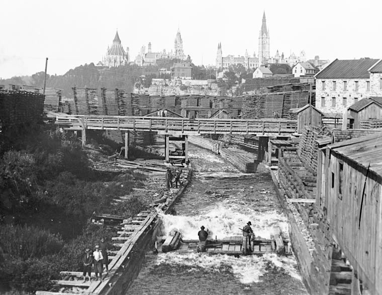A timber slide was a device for moving timber past rapids and waterfalls.  The image here is of the main timber slide at Ottawa looking toward Canada’s parliament buildings. The men are riding a timber crib, which would carry up to 50 logs tied together down the chute.  The ride was very fast and hilariously wet, which often attracted visiting dignitaries.  In 1850, it was reported that up to 500 cribs went through this slide in one day.  The logs were on their way to Montreal for shipment overseas.  

Studio of William James Topley (1845-1930), Ottawa portrait photographer. View full size.   