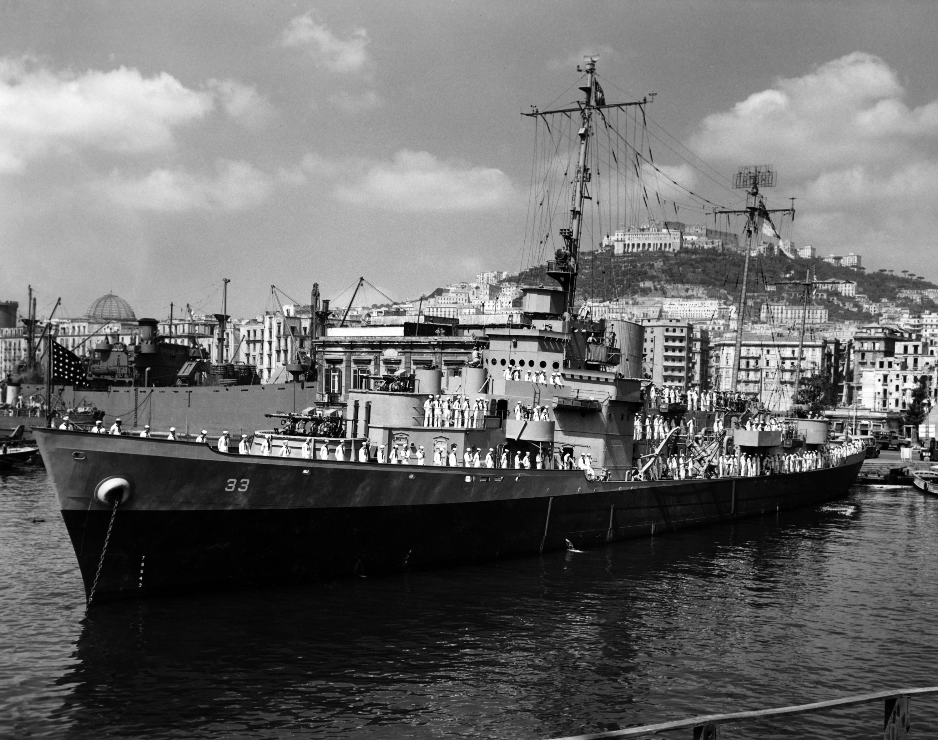 This photograph is of the USS Duane and its crew in Naples, Italy. According to the official USCG history, the ship was docked in Naples approximately six different times between May 1944 and August 1944. The longest stay being from July 30th until August 9th. It is likely that the photograph was taken during this ten day stretch. Although it is not marked, Dale Rooks was the likely photographer for this image as he took several others in John Baker's Warbook in the weeks after this was likely taken.

On the left hand side of this photo, you can see a Dome which is the San Francesco di Paola Church. The building in the middle right of the photo (on top of the hill) is the Certosa di San Martino, which is now a museum. A current image can be compared here. View full size