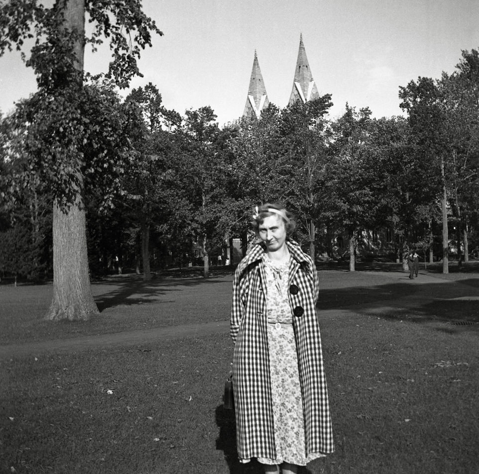 Lady in plaid posing in the park with a couple of rooftops marked with V. Not sure if it's part of the design or not. From my negatives collection. View full size.