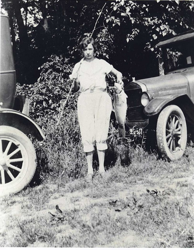 This is my wife's grandmother holding up her catch (looks like a big carp!) after a day of fishing with a cane pole in 1917 on the Little Miami River near Cincinnati, Ohio.  She was 17 years old at the time and lived until 1969. The cars look like a couple of Model T Fords. Those old "flivvers" would go anywhere! View full size.
