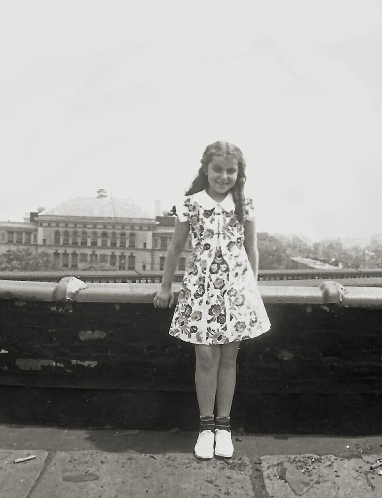My then-seven-year-old future mother poses on the roof of her apartment building (1027 44th St, Brooklyn NY) for one of her parents to take her picture. She lived in that same apartment from birth until she married my father in 1951.
What is most interesting about the childhood  pictures of my mother from this era is that she is always in the same dress. I am quite sure, unlike Little Orphan Annie, she had more than one dress to wear. But somehow the same one was chosen for every photo.