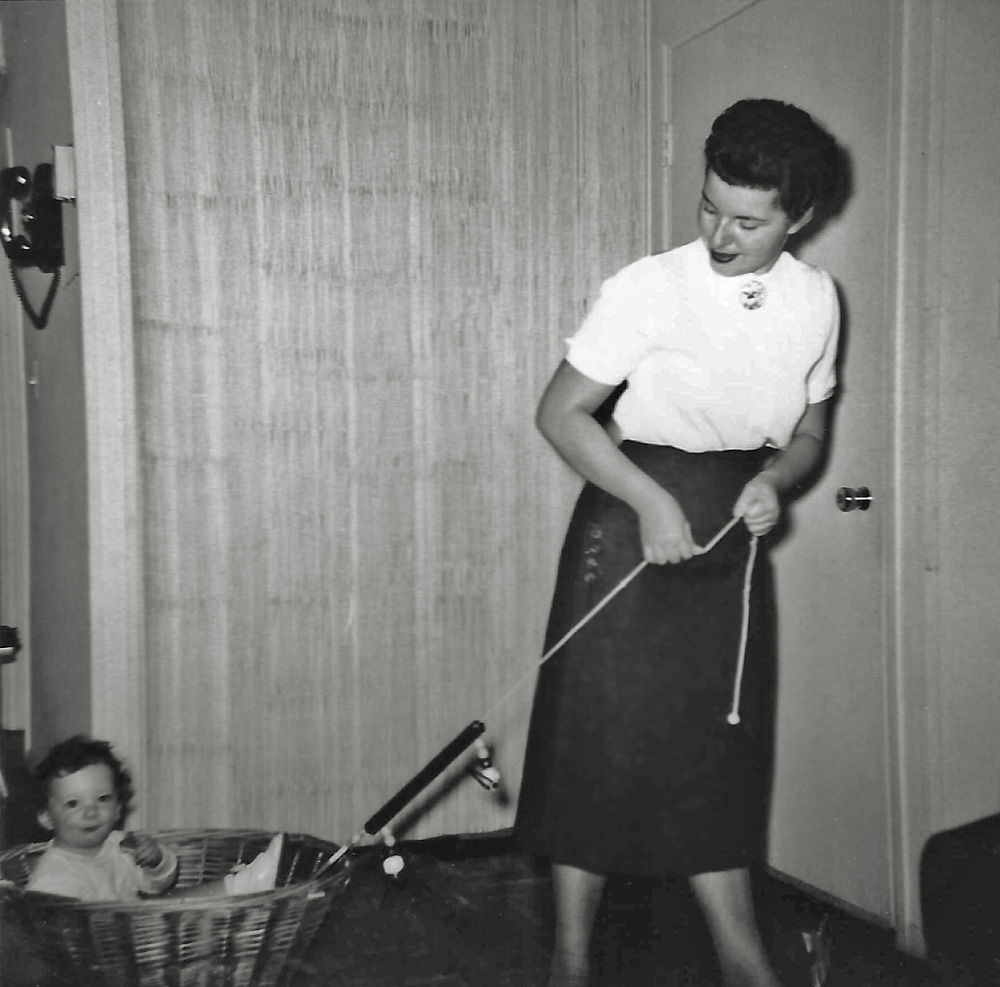I haven’t a clue what the story of this playful mother and baby snapshot is about. I only know that my mother is pulling a wicker basket, I am sitting in it, and somebody took a picture of that. I also know the front door to this Levittown, Pennsylvania house is beyond her shoulder, and beyond that is a bamboo curtain hiding the washer and dryer. As far as I can remember we never owned such a wicker basket. She had a wheeled wagon for laundry and a stand up hamper for dirty clothes. I also know that my mother was not playful. She just wasn’t.  My theory is, that since all Levittown houses looked exactly alike, we are in some neighbor’s kitchen and the young mothers who had gathered with their baby boom babies, to socialize, came up with this activity and basket.
