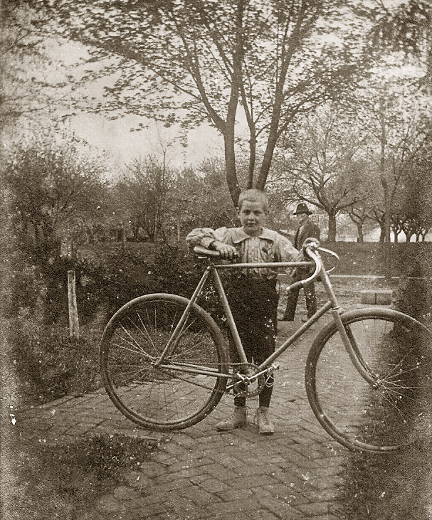 This kid is named Jay Smiley and walking in the back is Jim Smiley. Jay and Jim must have been out for a bike ride in Shelby, Ohio, where the picture was taken. The year is around 1895. View full size.