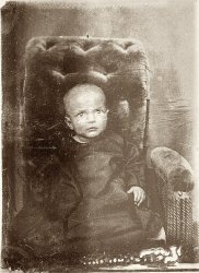 Tintype of an infant dressed in dark clothing.  Babies were usually dressed in white. Could the family have been in mourning?