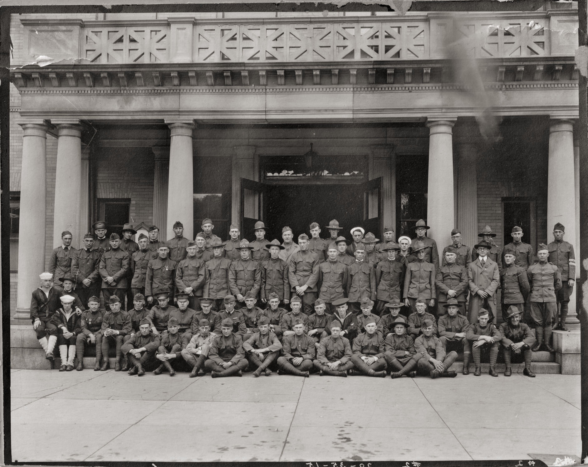 The photographer was Woodhead Photo Co. of Springfield, Massachusetts. Unknown where the photo was taken. It looks like different branches of the military are represented. 9th man from the left 2nd row...could that be Eddie Rickenbacker? He's the only one with wings above his pocket. Perhaps someone may recognize the building.