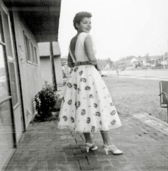 My mother designed and sewed this dress for herself in the late 1950's. I am guessing, based on the hem length, around 1958. She then had my father take her picture. Her intention was to show off her design and dress-making skills. But what this picture really shows is the mid century modern and still new world of Levittown, Pennsylvania during the first few years after it was built in 1953. Every house got two fruit trees and two pine trees that were basically single stalk sticks. With no landscaping the lots look huge, but they are only a quarter acre. Brick patio was an owner added modification. (In other words my father laid those bricks out in a bed of sand). She is standing at 110 Dogwood Drive, and you are looking diagonally northwest at the homes with lower street numbers. View full size.
Nice view!A pretty woman, your mother, in a dress with a daring plunging back!
(ShorpyBlog, Member Gallery)