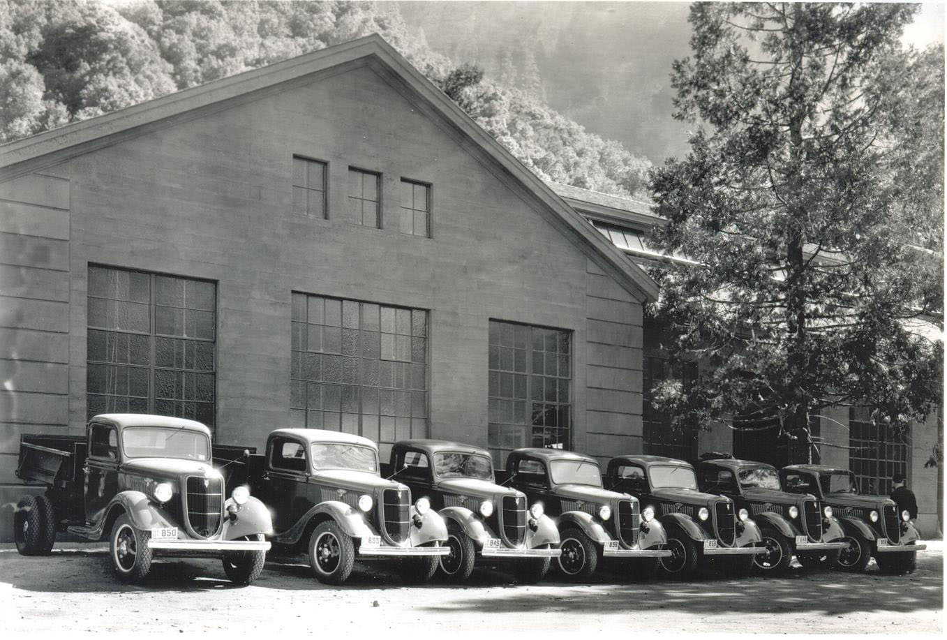 I believe these are brand new 1936 Ford Model 51 trucks parked in front of the Yosemite Machine Shop (National Park Service) in the Yosemite Valley. Appears to be Department of the Interior license plates. This side of building is still in use by maintenance personnel. The other side of the building, which is out of sight on the right, houses the fire station and jail. 